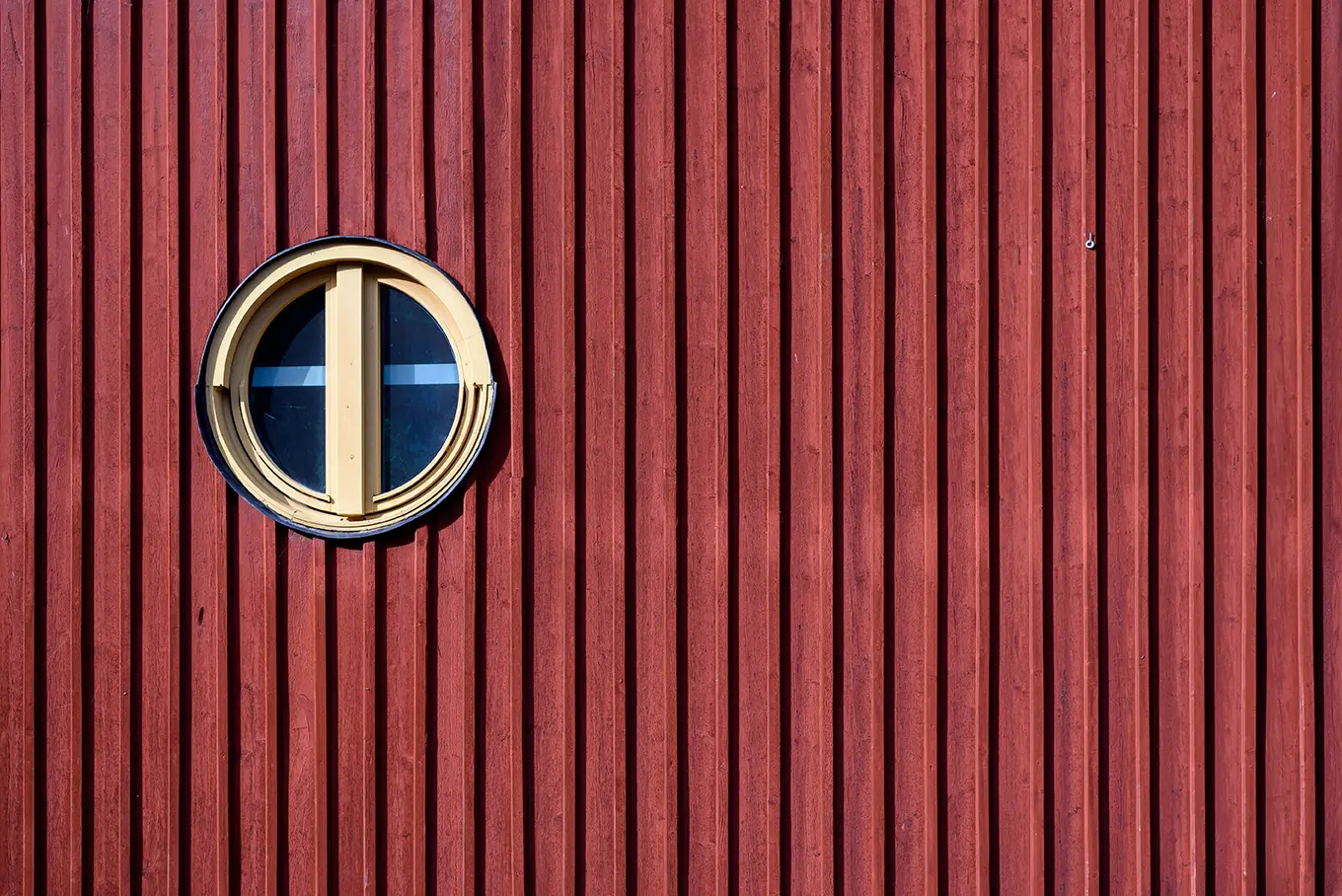Eine Nahaufnahme einer röten Holzfassade mit einem gelben runden Fenster