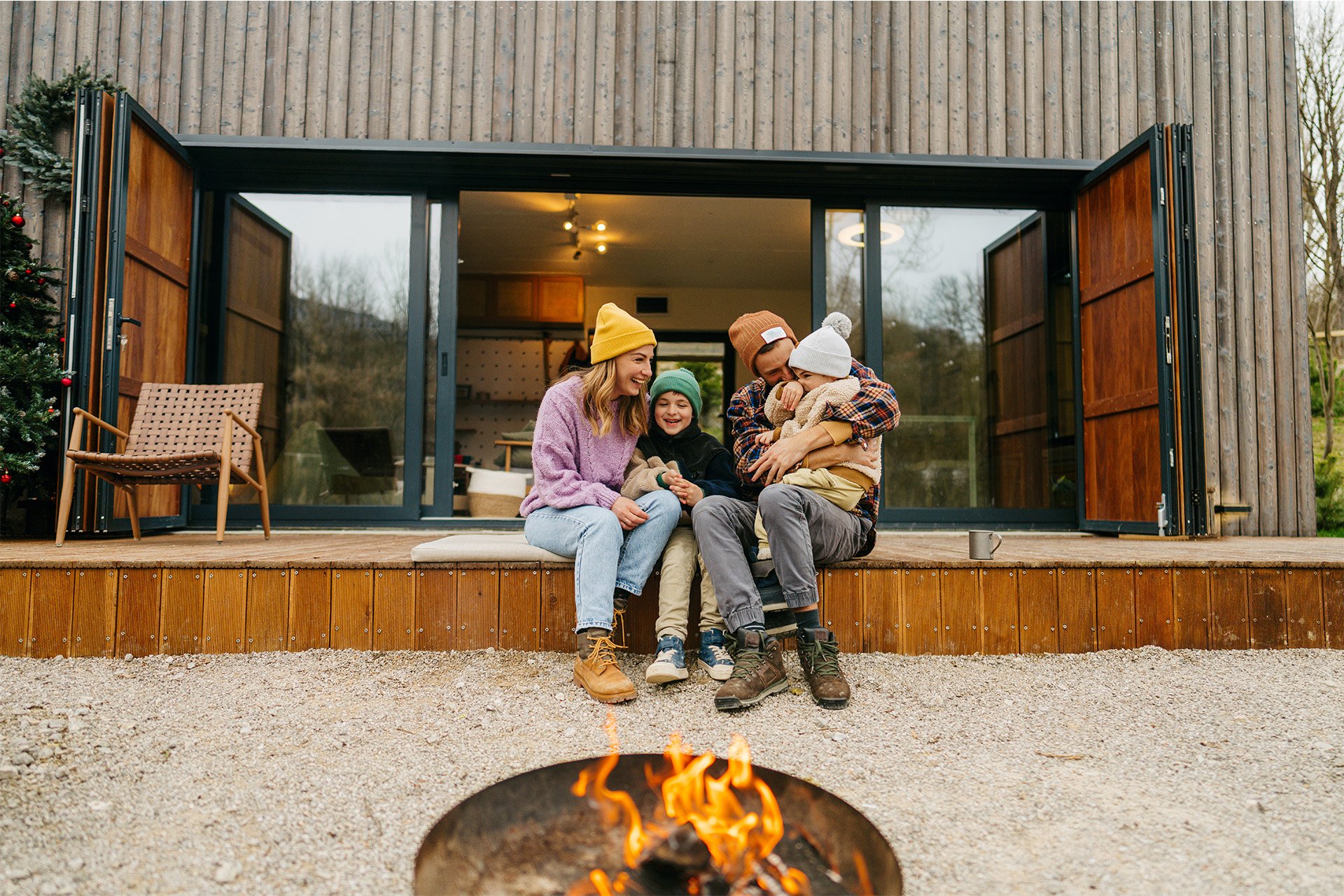 Familie sitzt entspannt auf einer Terrasse vor einem Holzhaus mit moderner Holzfassade.